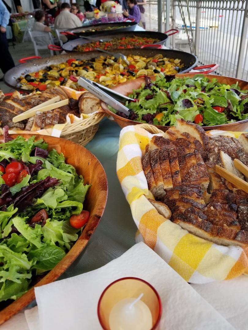 a table with bread, salad, and paella