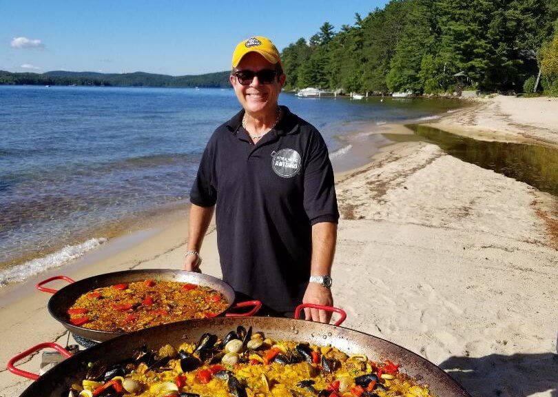 a man posing with paella pots on a beach