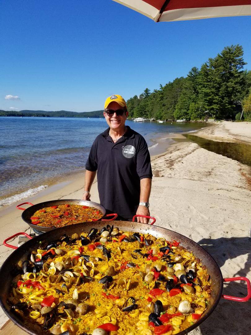 a man posing with paella pots on a beach