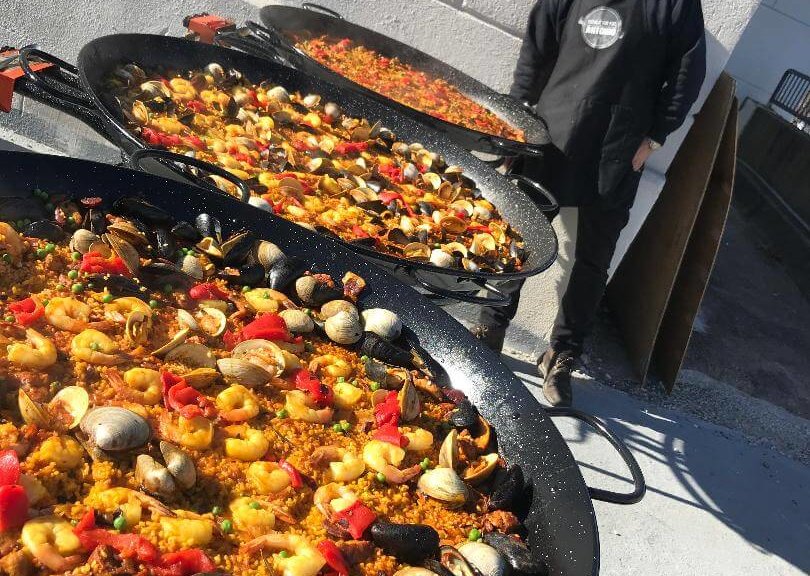 a man posing with three pans of paella