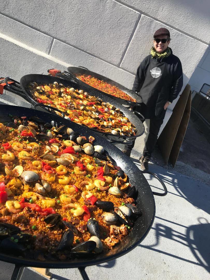 a man posing with three pans of paella