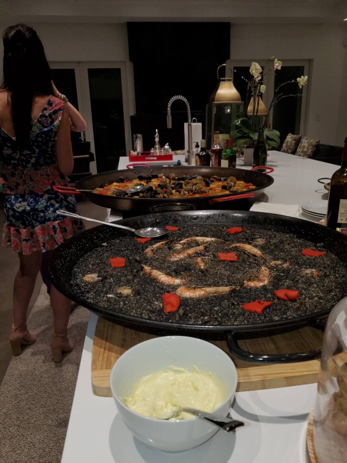 a woman standing near two pots of Paella on a table