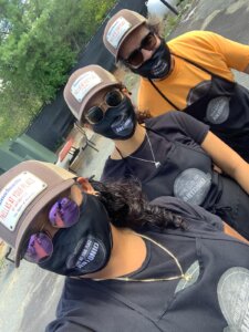 Three people wearing masks and hats outdoors.