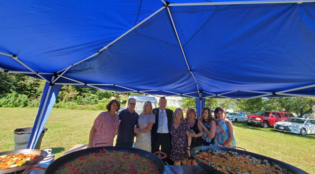 six women and two men posing for a picture near food pans